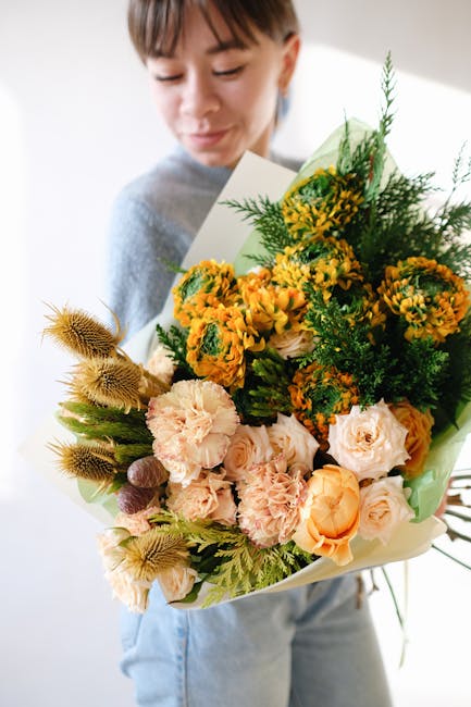 A young woman is holding a large floral gift arrangement featuring a variety of fresh flowers, including peach and cream roses, bright yellow and orange marigolds, and green foliage, arranged in a lus