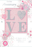This anniversary card is presented in close detail, its design blending soft pastel pinks and silvery greys to create the feeling of a cherished keepsake, like a hand-written love note tucked alongside flowers delivered in Blackwall. At the centre, the word LOVE is arranged in bold, raised letters that invite touch, each one coated in a fine, shimmering glitter that glows softly rather than dazzling. The letter O is replaced by a silver-toned heart, also textured and slightly embossed, giving the focal point an extra sense of warmth and intimacy.

Radiating out from this central motif, delicate blossoms in blush, mauve, and pale ivory seem to unfurl across the card. The flowers are illustrated with flowing, almost watercolor softness, petals shaded lightly so they appear to overlap and curl. Slender vines, tiny leaves, and subtle swirls flow around the blooms, their lines so fine they resemble the elegant stems and tendrils a florist might carefully arrange in a romantic bouquet bound for a nearby riverside apartment. Tiny butterflies and small petal details add movement and a hint of whimsy, recalling the gentle grace of an English spring garden.

The background is a serene wash of pastel pink, with slight variations in tone that give the impression of textured artist's paper. Phrases such as On Our Anniversary and I love you today and always are set in a refined script, the letters looping gracefully as if written by hand. Together, the tactile glitter, soft colours, and floral motifs create an atmosphere of intimate celebration: a visual expression of enduring romance, perfect for marking another year of shared life and love in the quiet corners of Blackwall.
